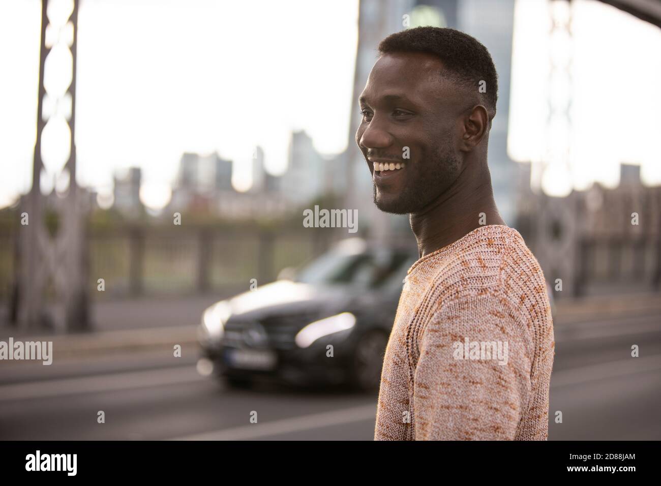 Schöner schwarzer Mann lächelnd wegschauen posiert auf der Straße. Mittlere Aufnahme. Geringe Schärfentiefe. Fokus auf Vordergrund. Stockfoto