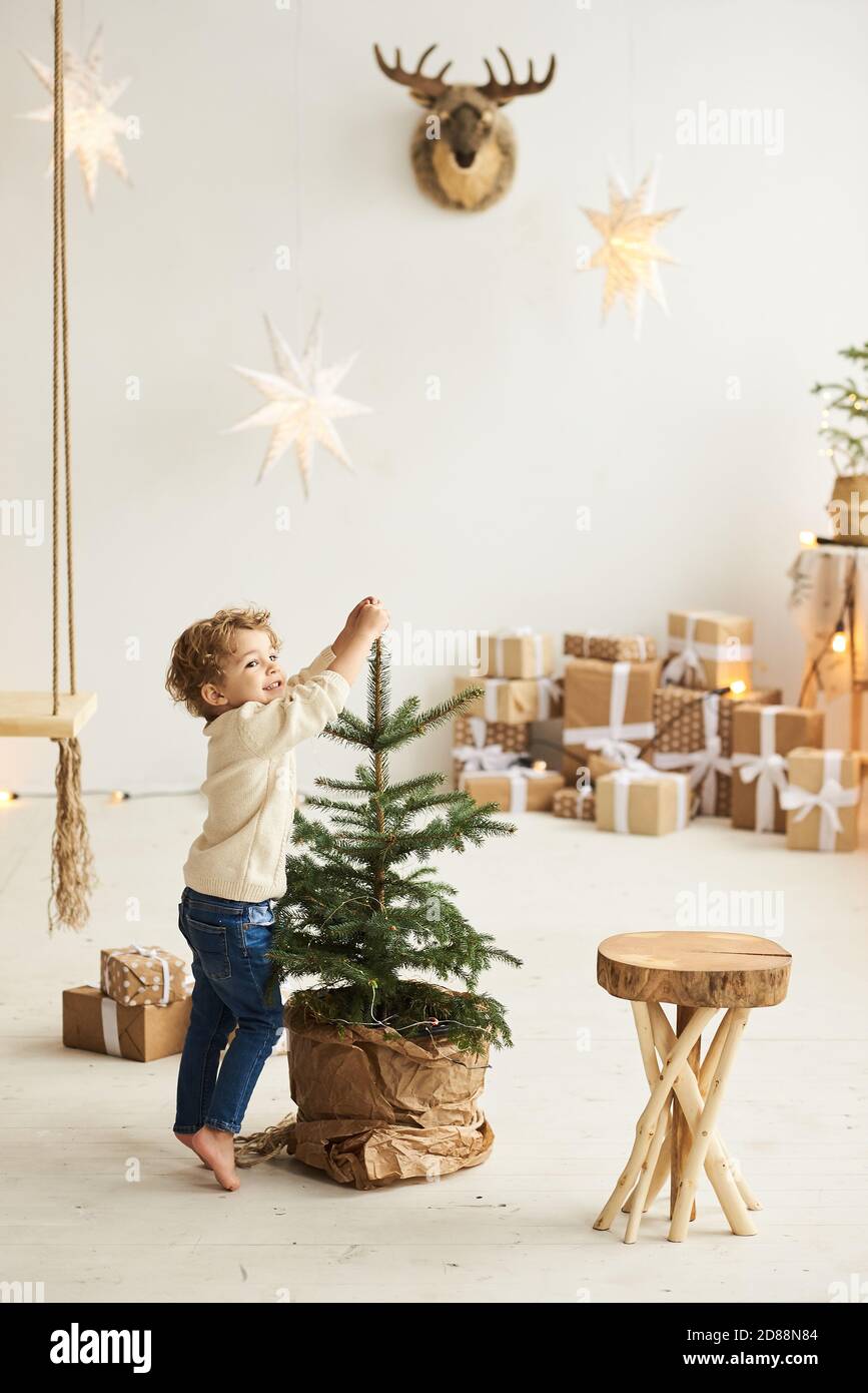 Schöner lockiger kleiner Junge schmückte einen Weihnachtsbaum in einem Weißes Zimmer Stockfoto