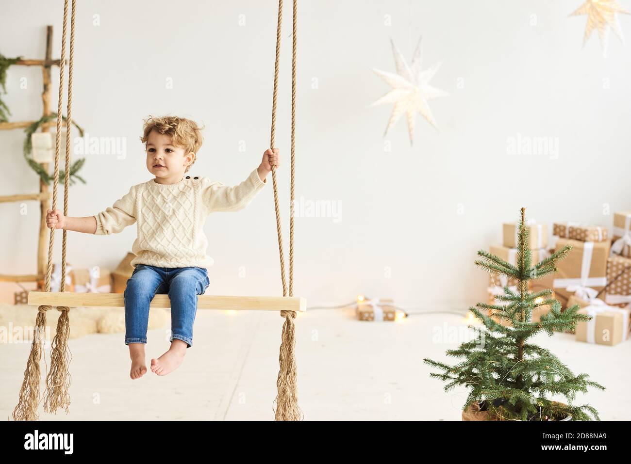 Schöner lockiger kleiner Junge schmückte einen Weihnachtsbaum in einem Weißes Zimmer Stockfoto