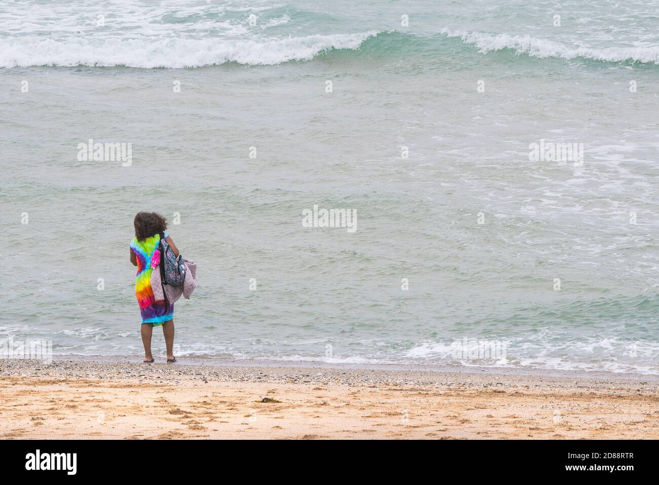 Ein Urlauber, der in einem bunten Kleid am Fistral Beach in Newquay in Cornwall auf einem Aufenthaltstag ist. Stockfoto