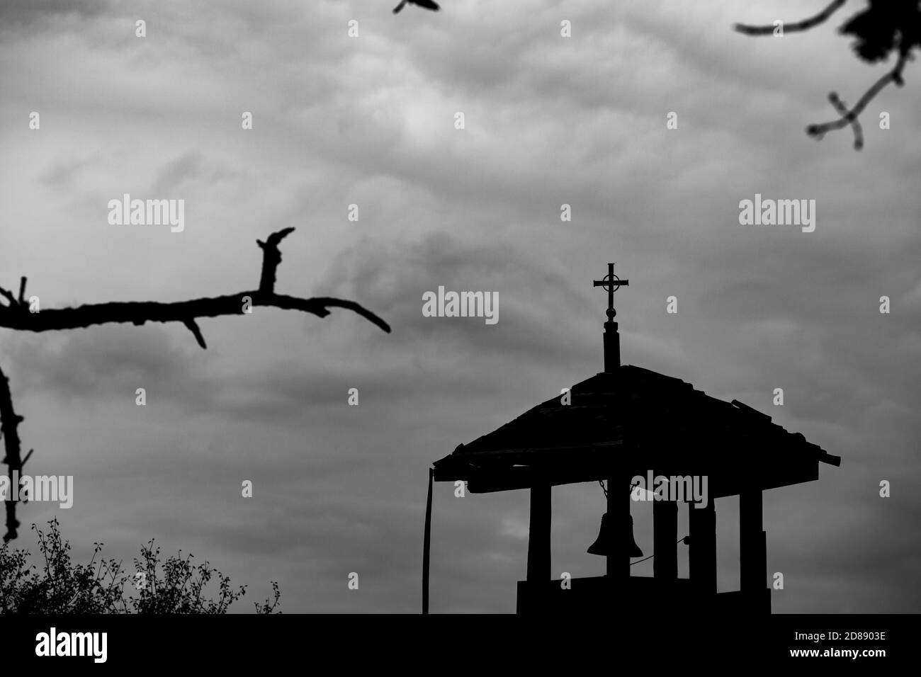 Selektiver Fokus auf metallischen Kreuz auf kleine alte Kirche Glockenturm am entfernten orthodoxen Tempel, Südbulgarien, bewölkten Herbsttag. Moody Darkness Silhouetten Bild Stockfoto