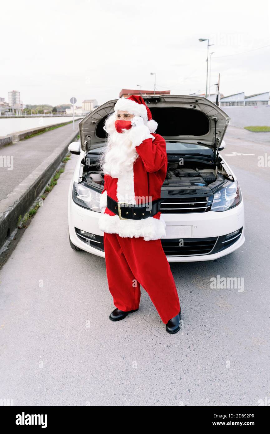 Porträt des Weihnachtsmannes im Gespräch mit einem besorgten Handy Mit der Haube geöffnet, weil sein Auto brach und Er kann die Geschenke der Kinder nicht ich liefern Stockfoto