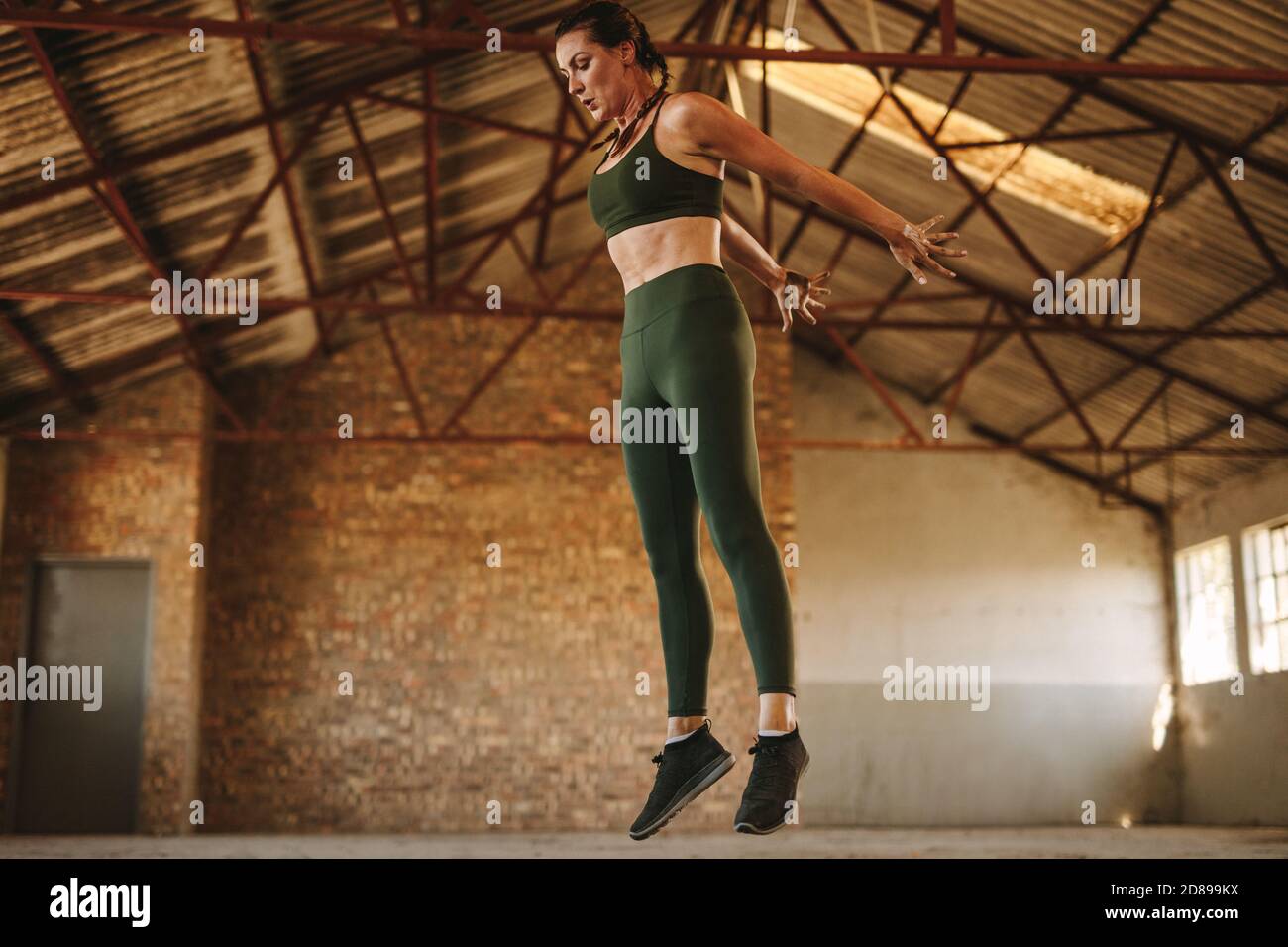 Sportlerin springt hoch. Gesunde Fitness Frau tun Übung im Fitnessraum im alten Fabrik Schatten. Stockfoto