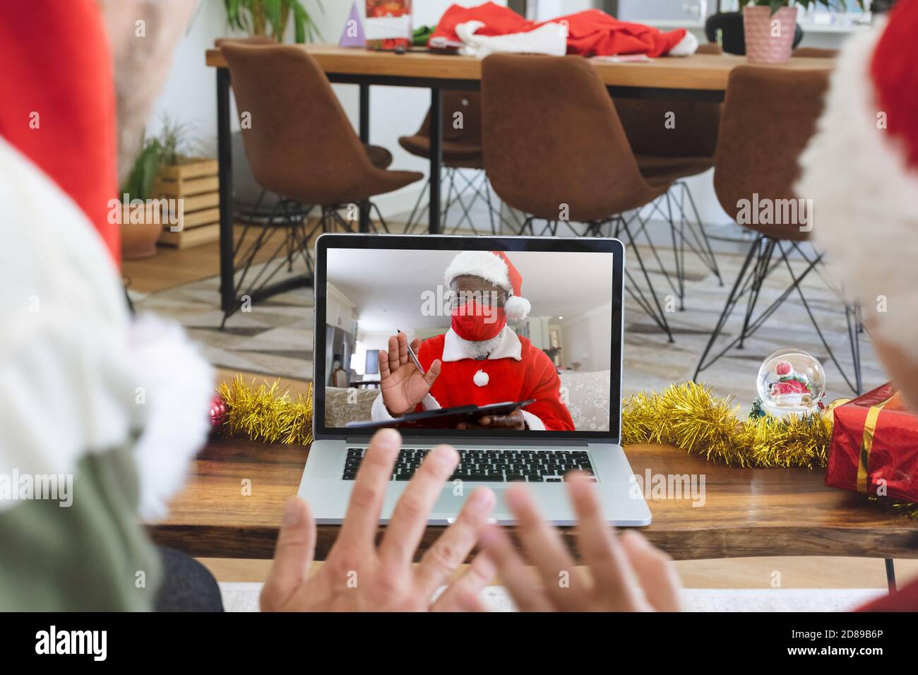 Rückansicht von Mann und Sohn in santa Hüte winken Während mit einem Videocall mit weihnachtsmann trägt Gesicht Stockfoto