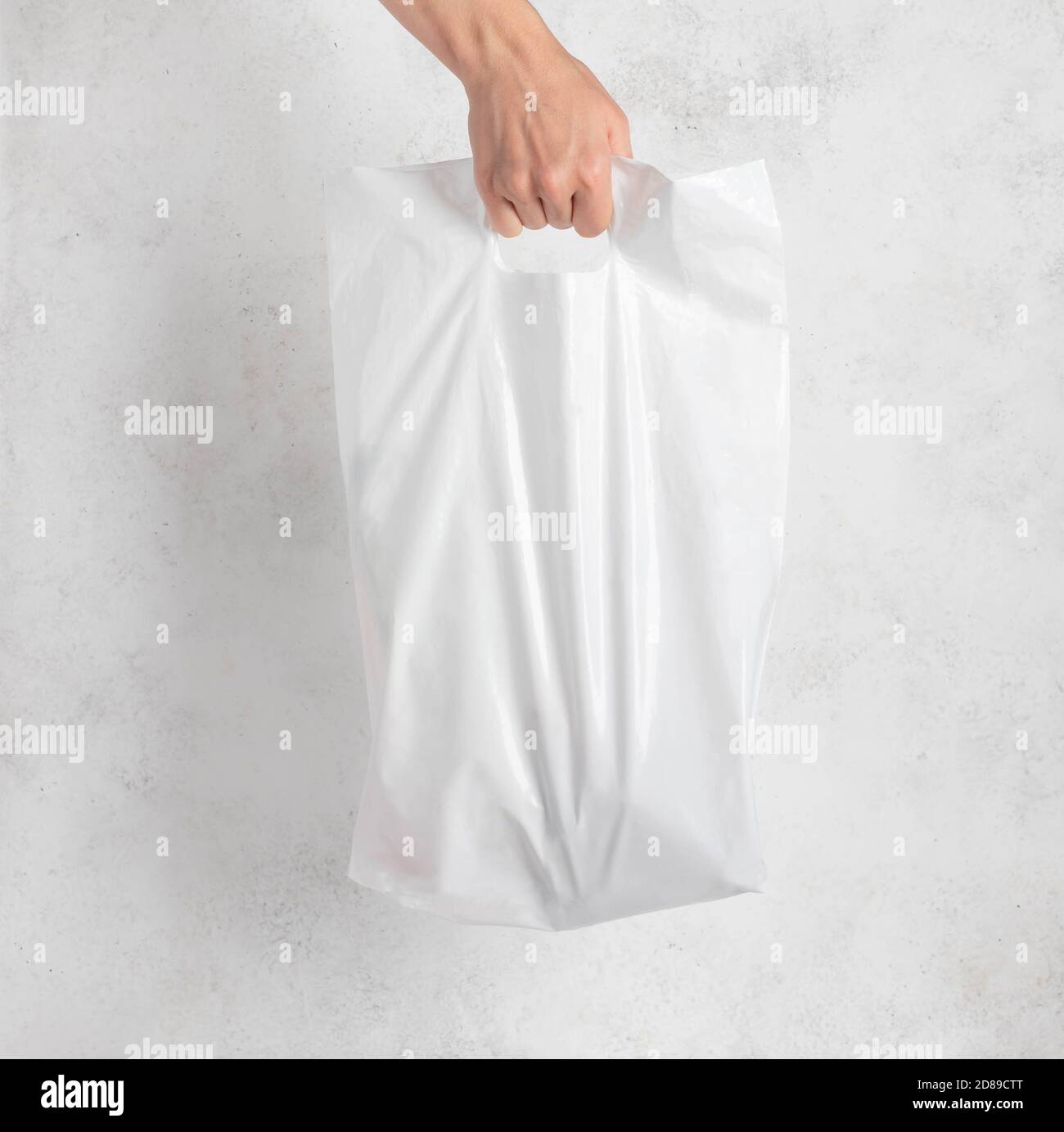 Weiße Plastiktüte, die von der Hand einer Frau gehalten wird. Heller Hintergrund. Stockfoto