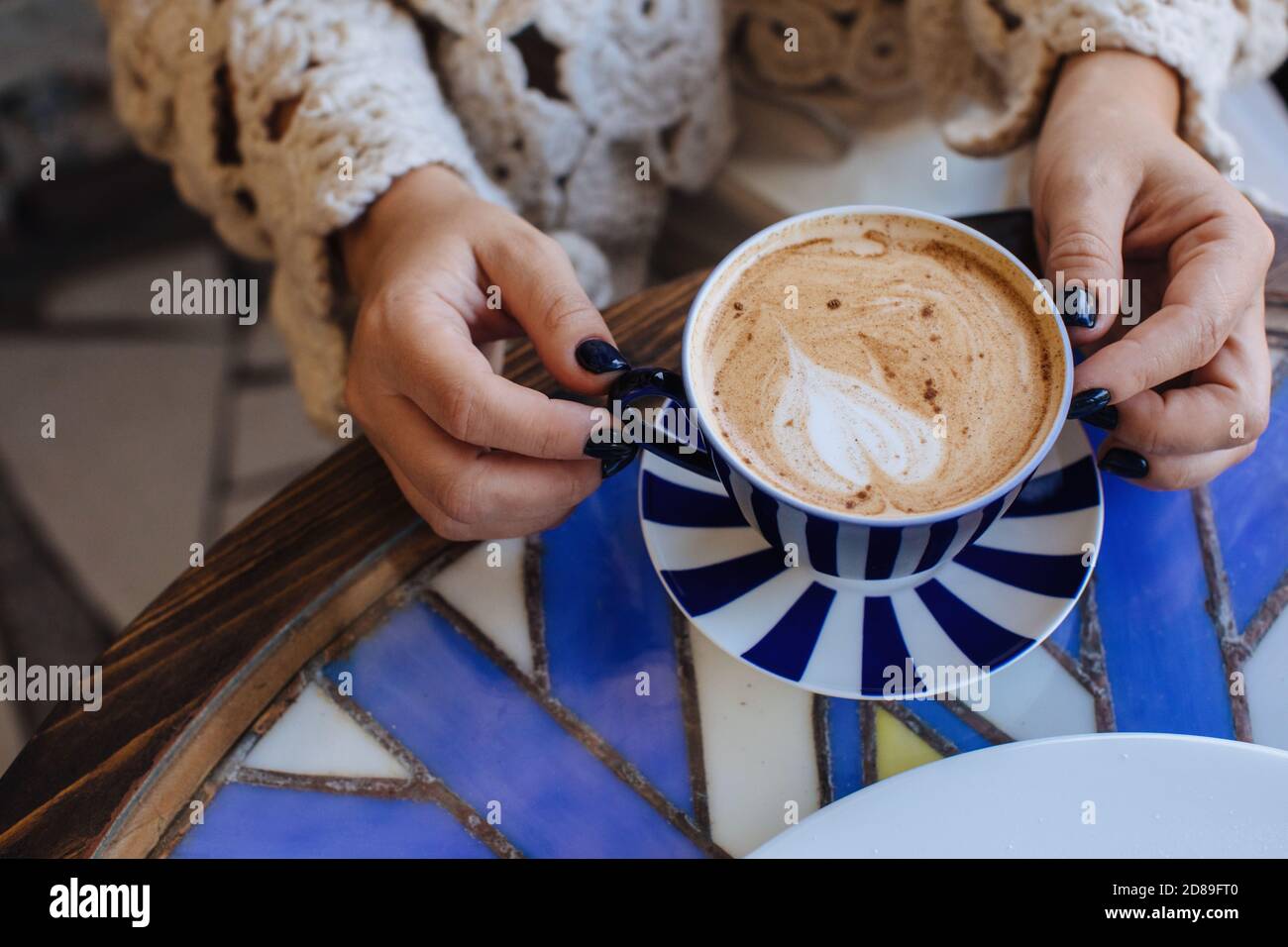 Nahaufnahme einer Frau, die an einem Tisch mit einem sitzt tasse Kaffee Stockfoto