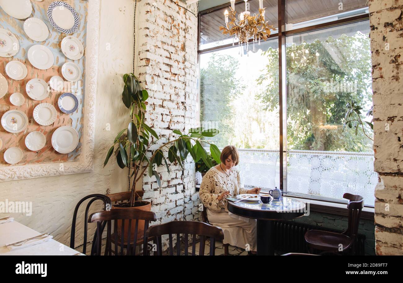 Frau, die in einem Café sitzt und eine Tasse Kaffee genießt Und ein Stück Strudel, während sie ihr Handy benutzt Stockfoto