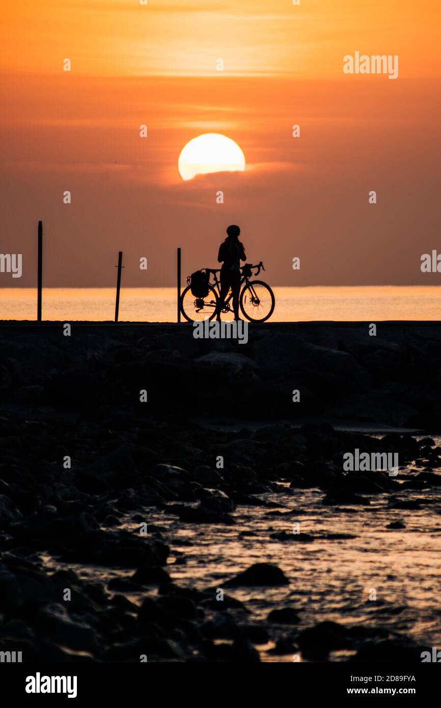 Silhouette eines Radfahrers, der bei Sonnenaufgang am Meer steht, Fuengirola, Malaga, Spanien Stockfoto