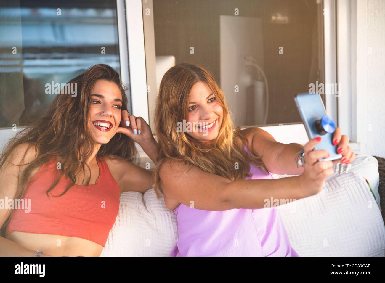 Zwei Freundinnen nehmen Selfie und lächeln auf einem Sofa Stockfoto