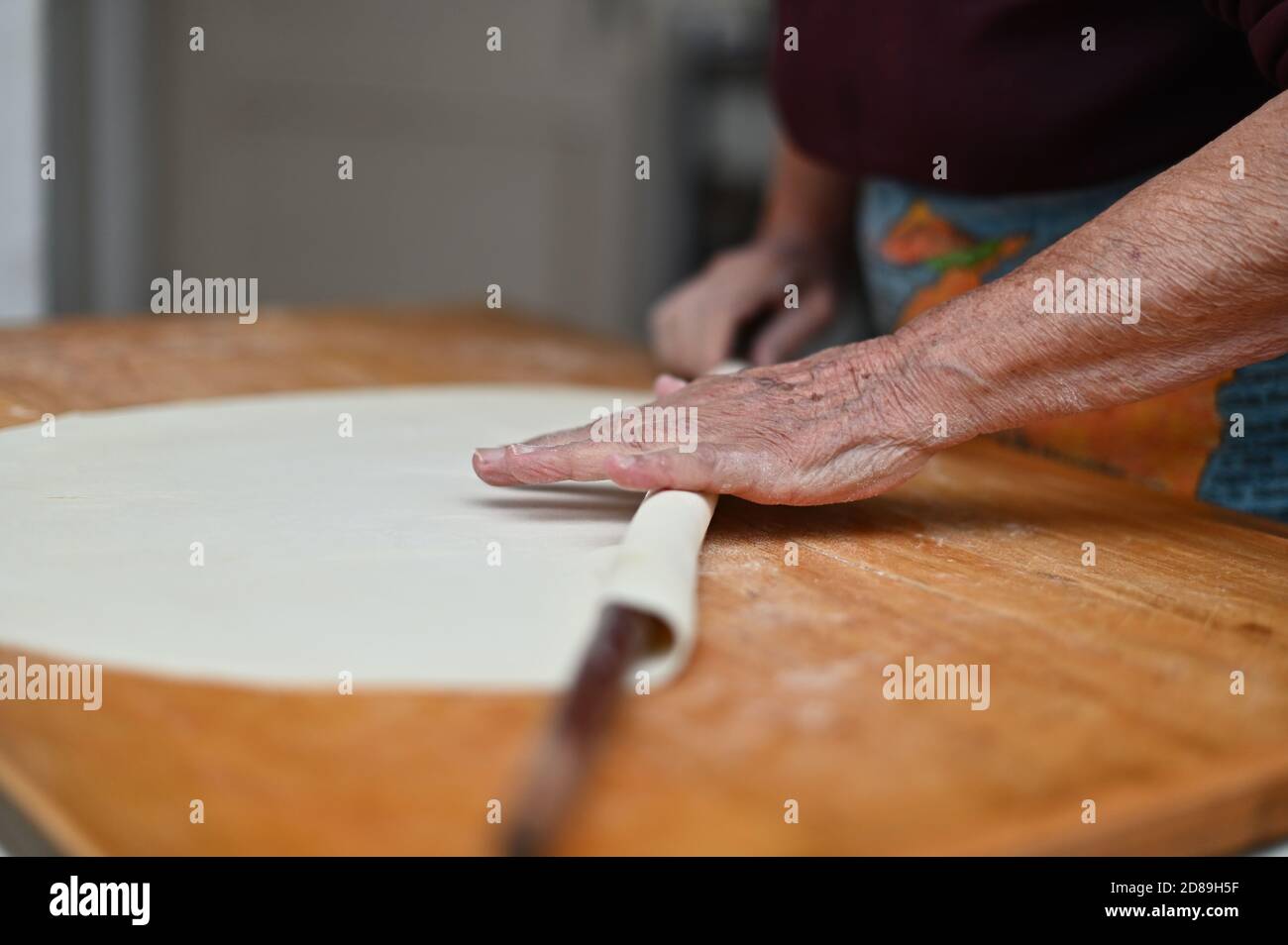 Nahaufnahme der Hände einer älteren Frau, die Teig ausrollt Ein Schneidebrett Stockfoto