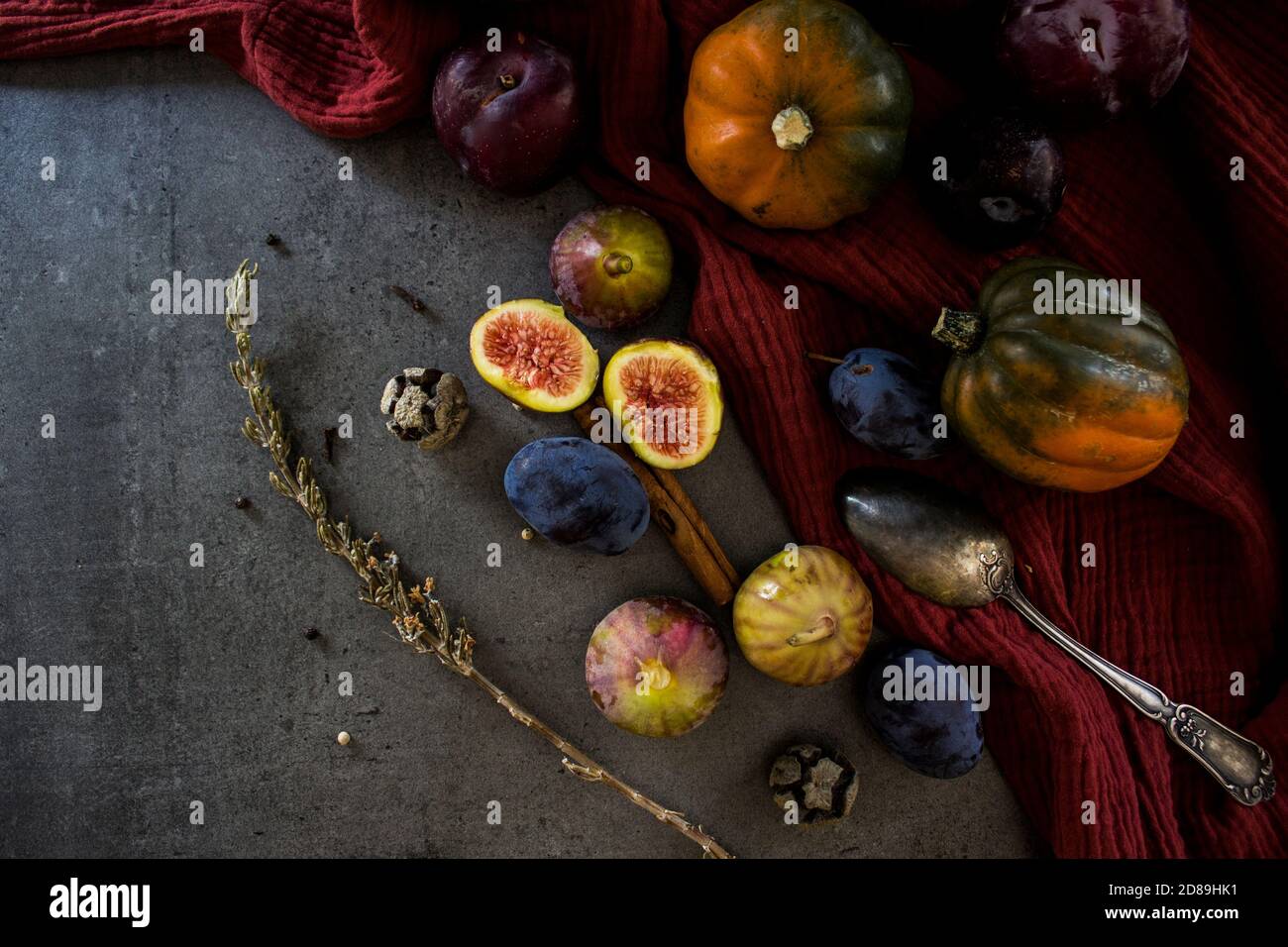 Frisches Obst und Gemüse auf dem Tisch. Edelsteinkürbis, Pflaumen, Feigen und Silberlöffel auf grauem Hintergrund. Draufsicht Foto der Herbsternte. Stockfoto