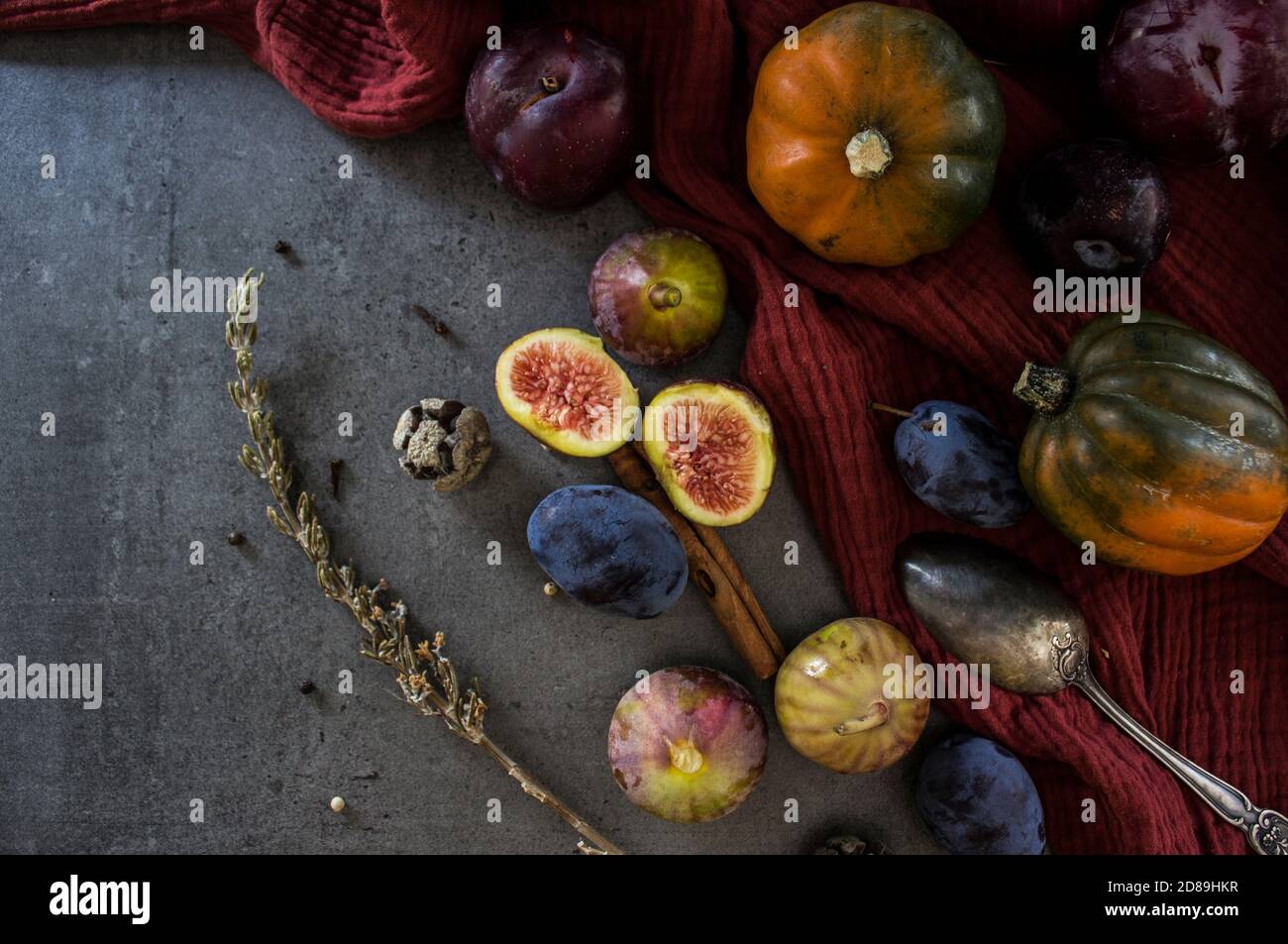 Frisches Obst und Gemüse auf dem Tisch. Edelsteinkürbis, Pflaumen, Feigen und Silberlöffel auf grauem Hintergrund. Draufsicht Foto der Herbsternte. Stockfoto
