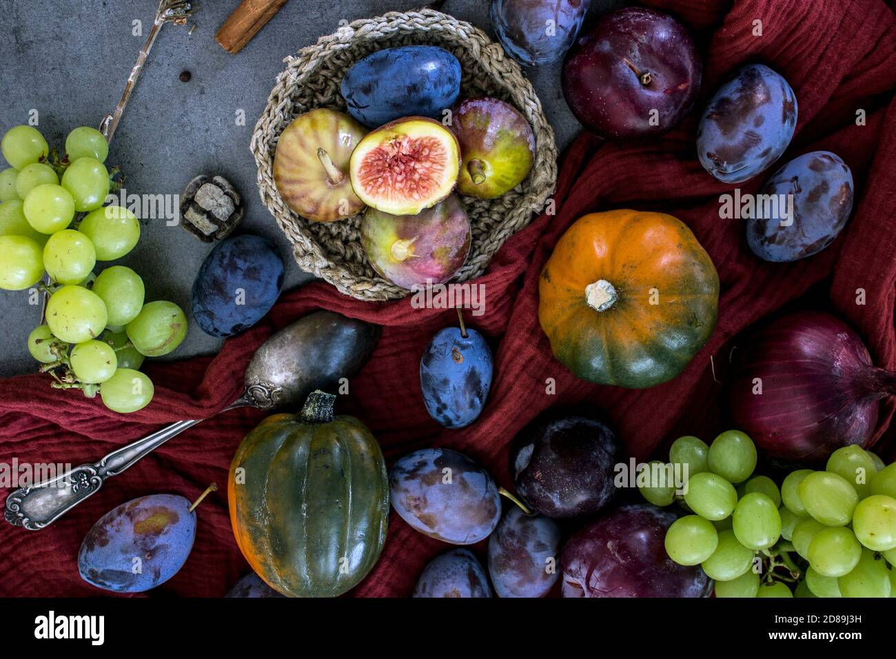 Frisches Obst und Gemüse auf dem Tisch. Foto von oben von Trauben, Kürbissen, Pflaumen und Feigen. Grauer strukturierter Hintergrund. Stillleben im Herbst. Stockfoto
