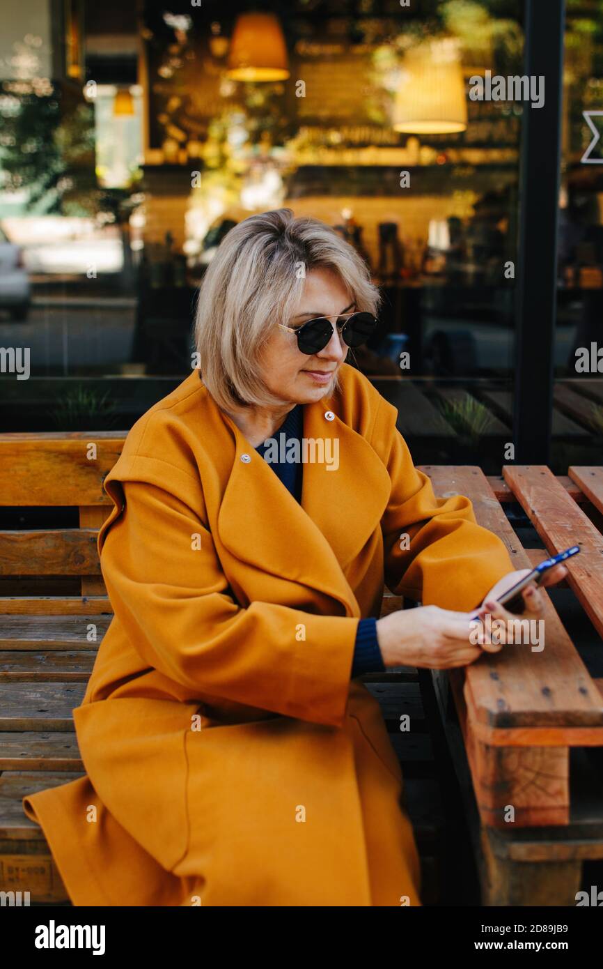 Porträt einer reifen Frau, die auf einer Bank sitzt und ihr Mobiltelefon, Russland, anschaut Stockfoto