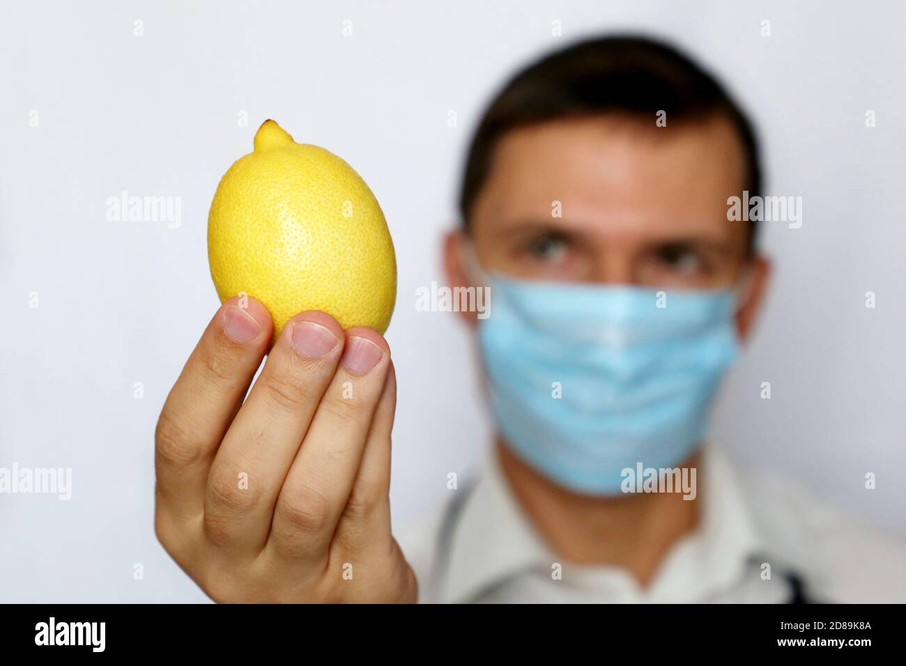 Influenza-Prävention, Mann in medizinischer Maske mit Zitrone in der Hand. Quelle von Vitamin C, Stärkung der Immunität während der Erkältungs- und Grippesaison Stockfoto