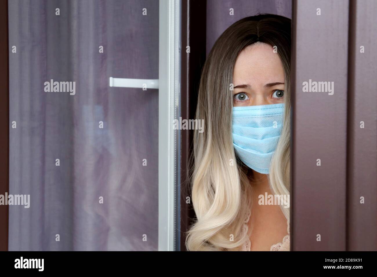 Coronavirus-Quarantäne während der covid-19-Epidemie. Besorgt Frau im Gesicht medizinische Maske schaut aus dem Fenster Stockfoto