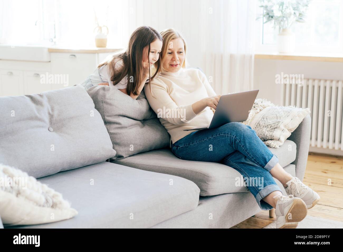 Mutter und Tochter verbringen Zeit zu Hause auf der Couch im Wohnzimmer mit einem Computer. Online-Kommunikation. Stockfoto