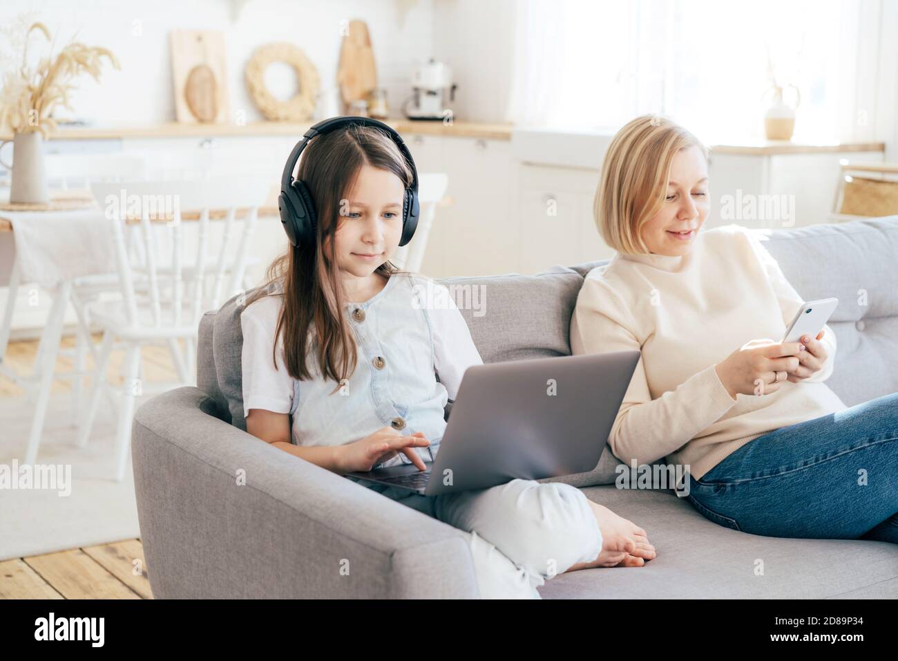 Mutter und Tochter sitzen auf der Couch und surfen in Gadgets. Stockfoto