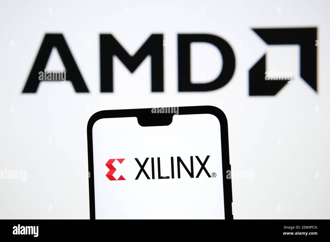 AMD übernimmt Xilinx, Konzept. XILINX-Logo auf der Silhouette des Smartphones in einer Hand gesehen und verschwommen AMD verschwommen Logo auf dem Hintergrund. Stockfoto