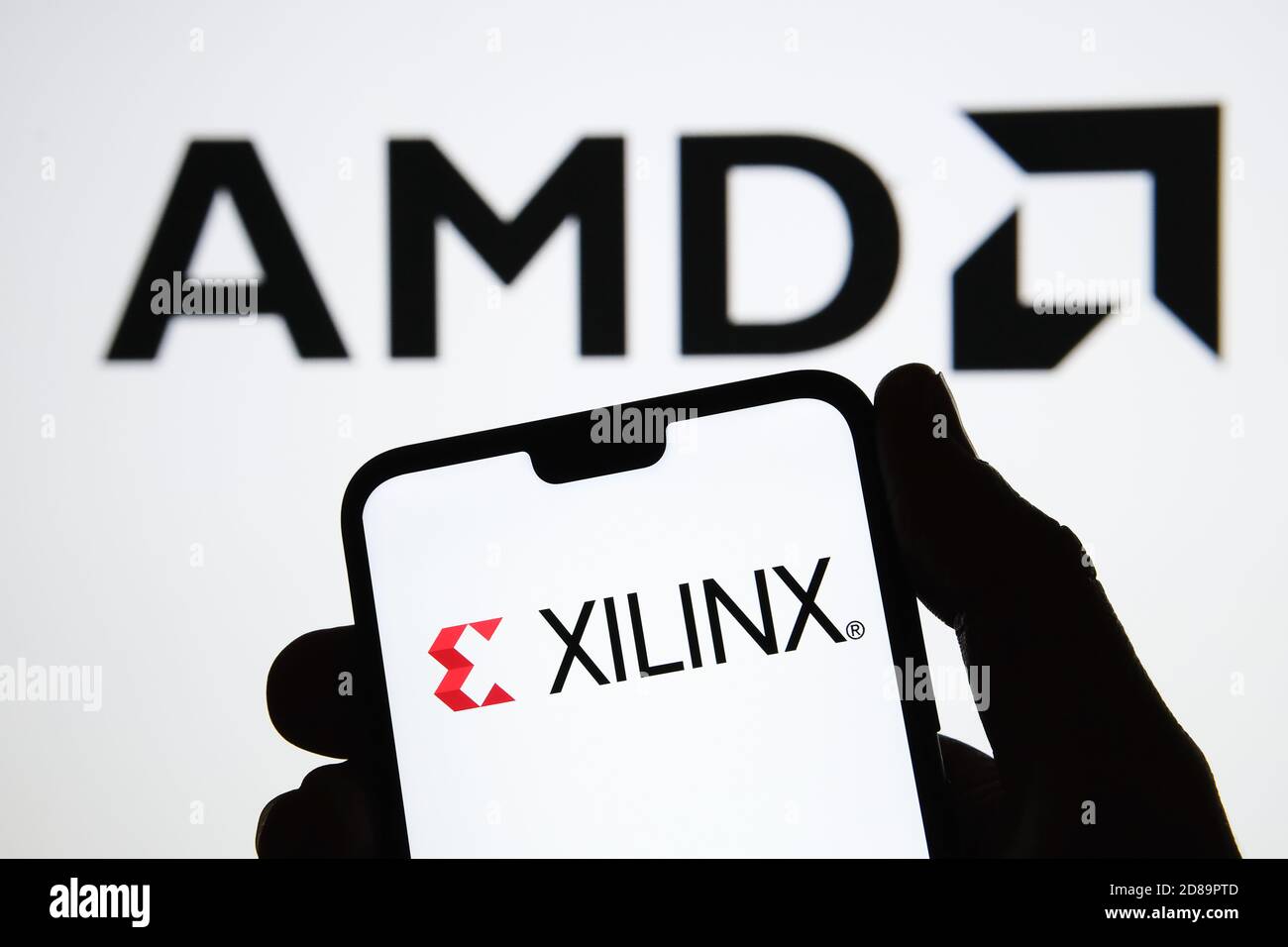 AMD Xilinx, Konzept. XILINX-Logo auf der Silhouette des Smartphones in einer Hand und verschwommen AMD gesehen Stockfoto