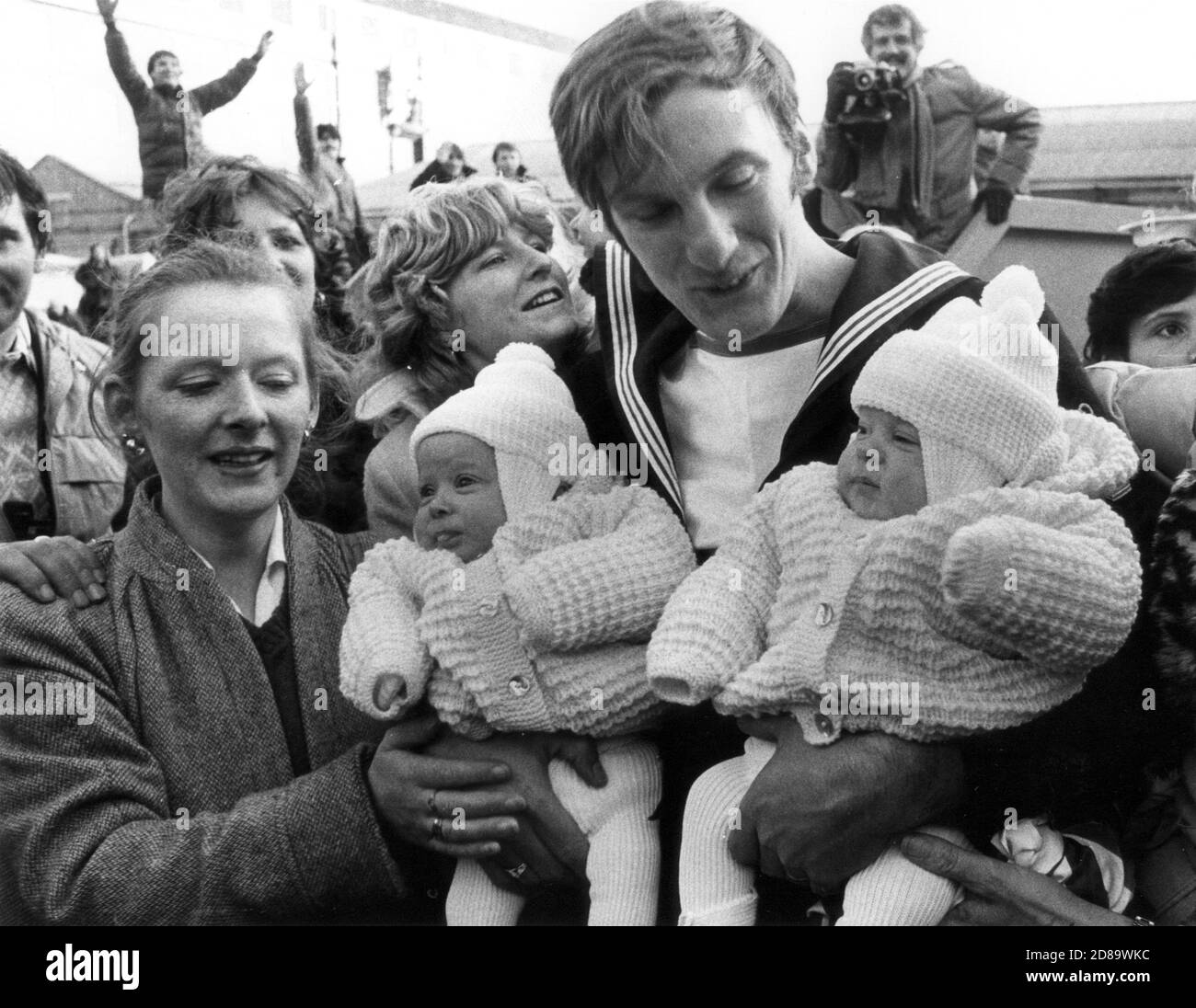 SEINE ZWILLINGSTÖCHTER ZUM ERSTEN MAL ZU SEHEN, IST NEU BEFÖRDERTER PETTY OFFICER ALAN DENHAM. ER WURDE VON DEN ZWILLINGEN CLAIRE UND DONNA UND SEINER FRAU CHERYL (22) BEGRÜSST, ALS HMS ILLUSTRIOUS AUS DEN FALKLANDS NACH PORTSMOUTH ZURÜCKKAM. 1982 Stockfoto