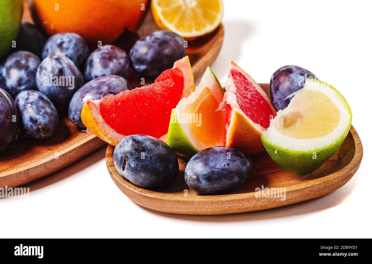 Grapefruit- und Pflaumenscheiben auf einer Holzplatte schließen isoliert auf weißem Hintergrund. Frische Sommerfrüchte Zusammensetzung. Stockfoto