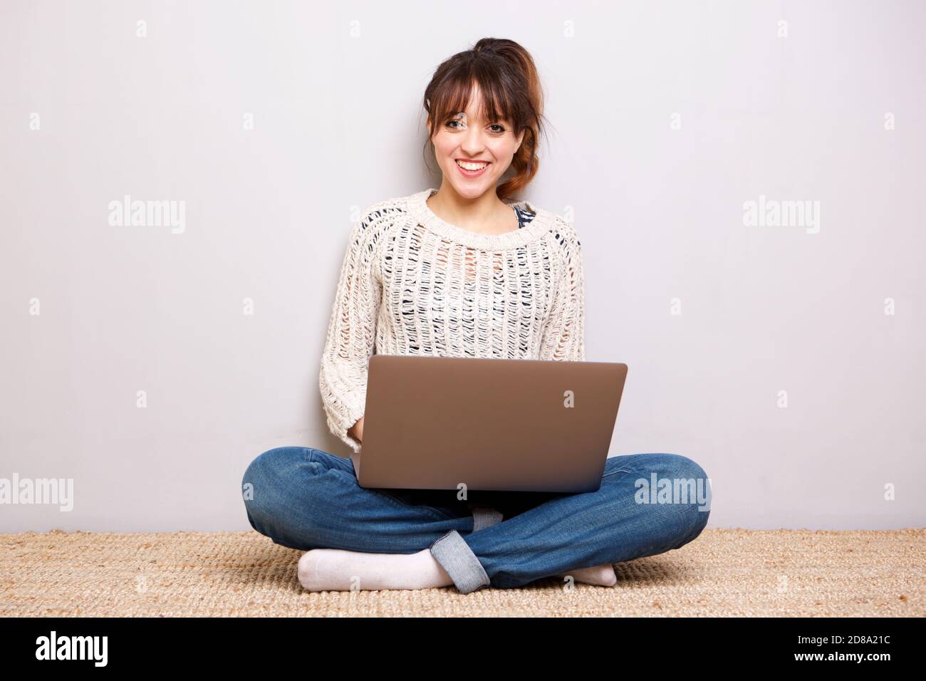 Porträt der glückliche junge Frau sitzt auf dem Boden mit Laptop Stockfoto