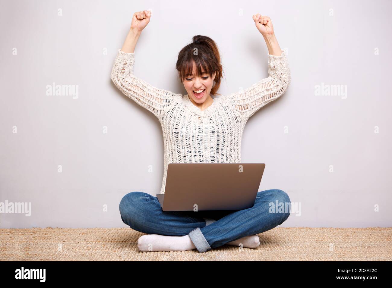 Porträt einer fröhlichen jungen Frau auf dem Boden mit sitzen Laptop und Arme angehoben Stockfoto