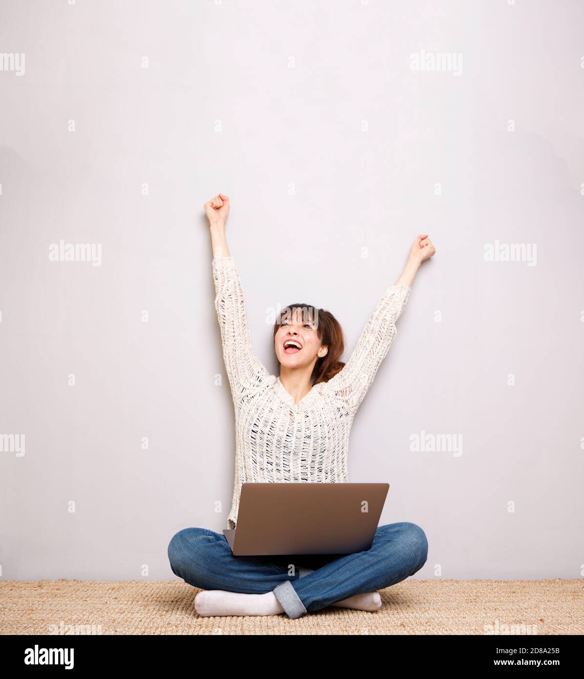 Porträt einer fröhlichen jungen Frau auf dem Boden mit sitzen Laptop und Hände angehoben Stockfoto