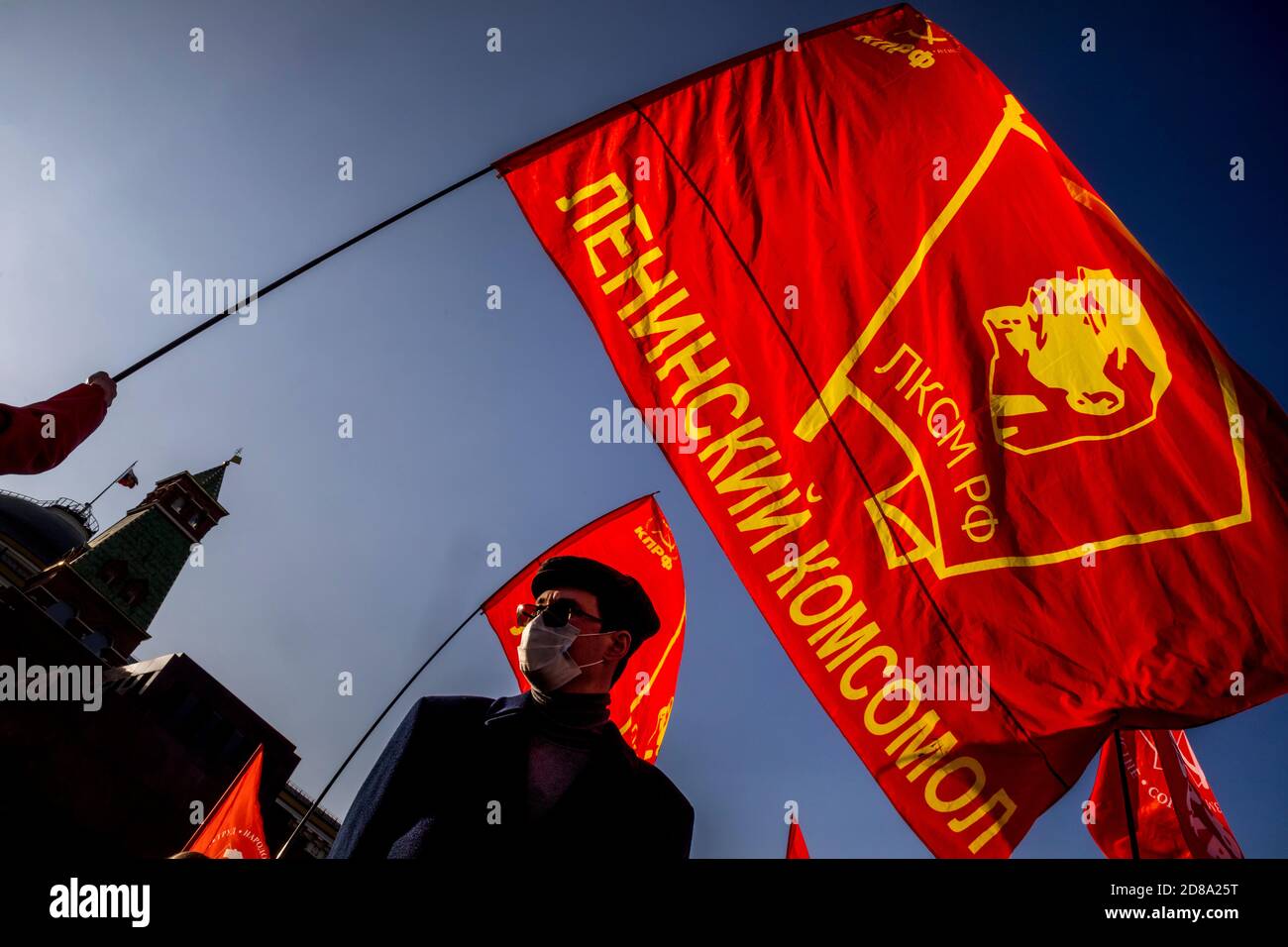 Moskau, Russland. 28. Oktober 2020 EIN Anhänger der kommunistischen Partei hält eine Rote Fahne mit Komsomolabzeichen, während andere sich auf dem Roten Platz versammeln, um den 102. Jahrestag des Komsomol, oder der All-Union Leninistischen Jungen Kommunistischen Liga, der sowjetischen kommunistischen Jugendorganisation, in Moskau, Russland, zu begehen Stockfoto