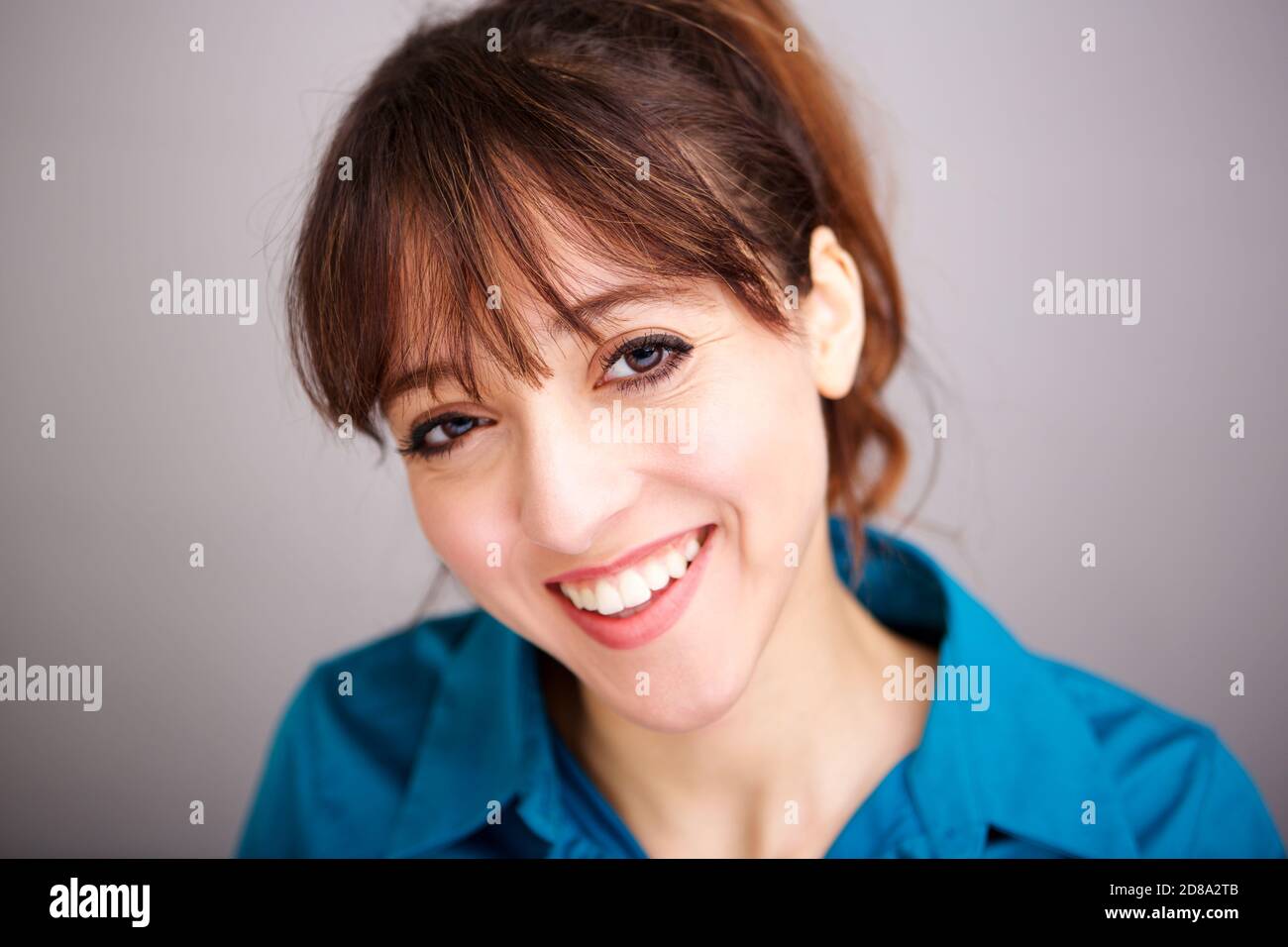 Nahaufnahme Porträt einer glücklichen jungen Frau lächeln gegen grau Hintergrund Stockfoto