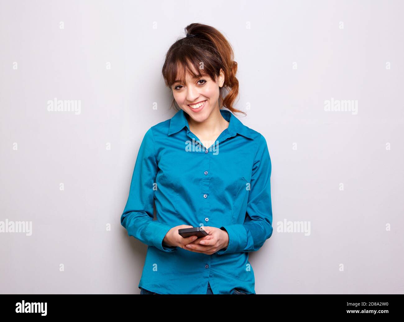 Porträt einer lächelnden jungen Frau, die das Handy gegen Grau hält Hintergrund Stockfoto