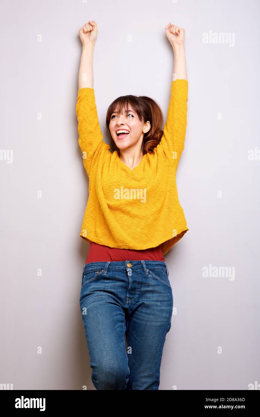 Porträt einer glücklichen jungen Frau, die mit erhobenen Armen lacht Grauer Hintergrund Stockfoto