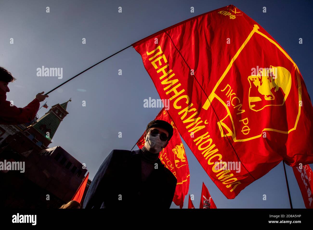 Moskau, Russland. 28. Oktober 2020 EIN Anhänger der kommunistischen Partei hält eine Rote Fahne mit Komsomolabzeichen, während andere sich auf dem Roten Platz versammeln, um den 102. Jahrestag des Komsomol, oder der All-Union Leninistischen Jungen Kommunistischen Liga, der sowjetischen kommunistischen Jugendorganisation, in Moskau, Russland, zu begehen Stockfoto