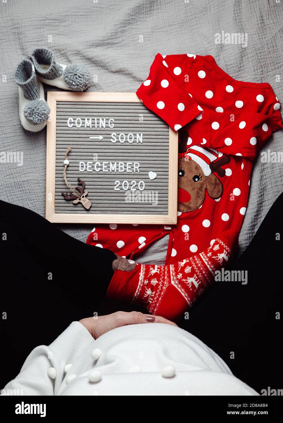 Schwangere Frau sitzt mit einem kommenden bald Dezember 2020 Baby Ankündigungszeichen. Demnächst Weihnachtskonzept. Schwangerschaftsbauch. Stockfoto