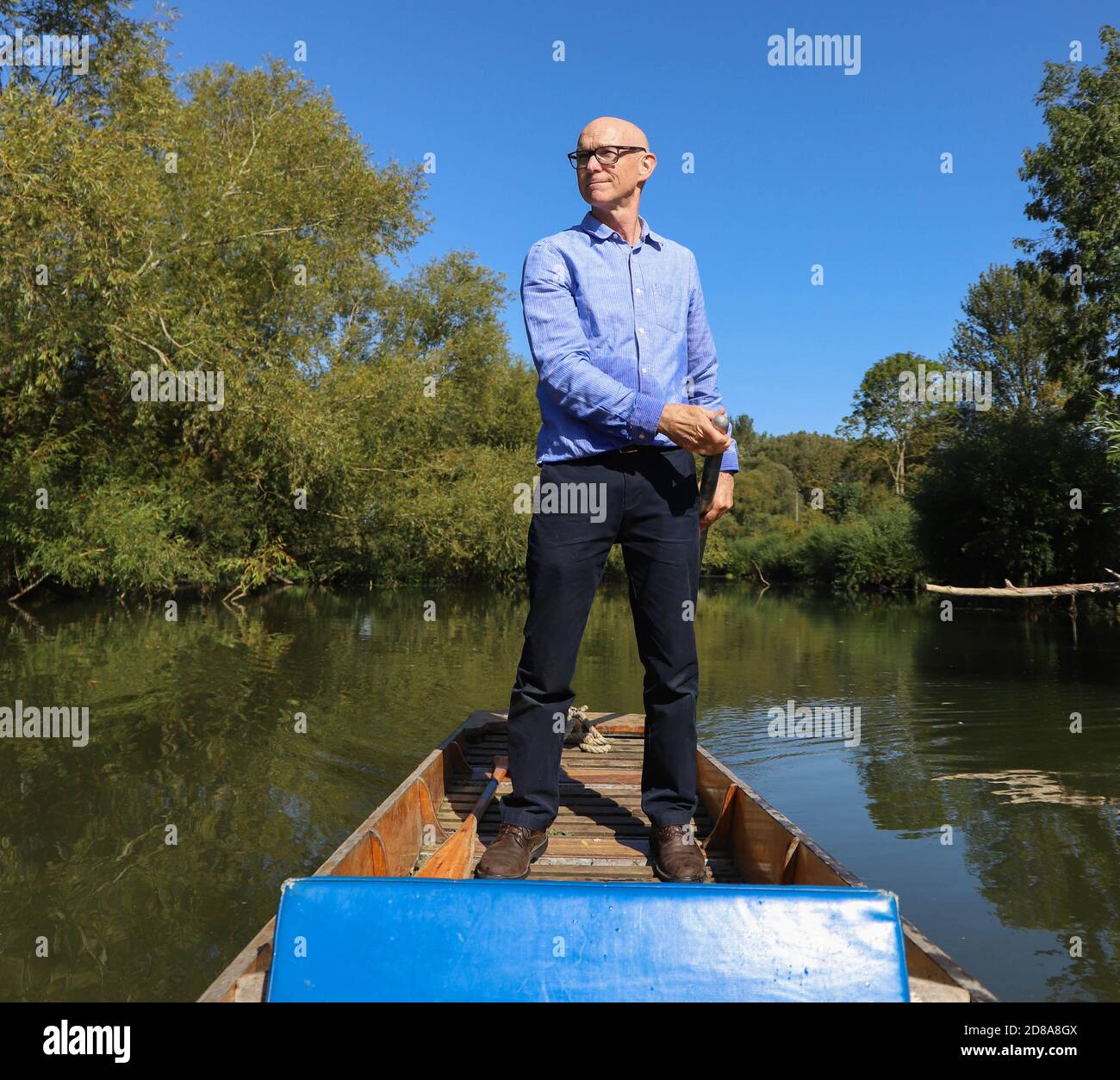 Zuversichtlich kaukasischen kahlen Mann trägt ein blaues Hemd und dunkel Blaue Hosen Navigation ein schmales Boot durch punting mit lang Pole die Cotswolds Stockfoto