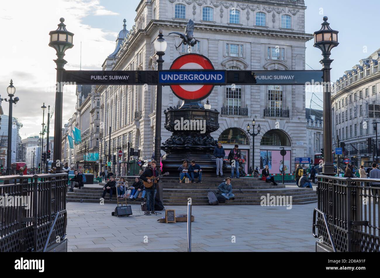 Ein Straßenmusiker spielt Gitarre am Piccadilly Circus unter einem Londoner U-Bahn-Schild an einem sonnigen Nachmittag. London Stockfoto