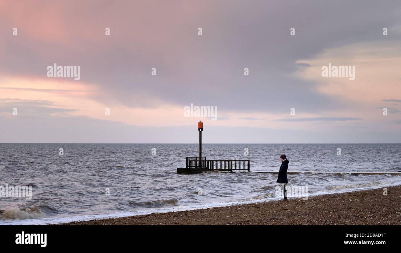 Junge Frau in warmer Kleidung, die nachdenklich auf See schaut Am Heacham South Beach ein beliebtes Küstenziel im Norden Norfolk bei Sonnenuntergang Stockfoto