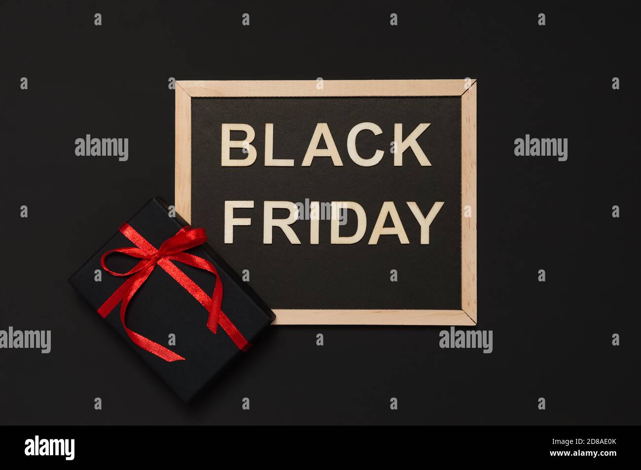 Black Friday Verkaufskonzept. Schwarzes Geschenk mit roter Schleife und Tafel mit Worten aus Holzbuchstaben auf dunklem Hintergrund. Flache Lay-Optik, Draufsicht Stockfoto