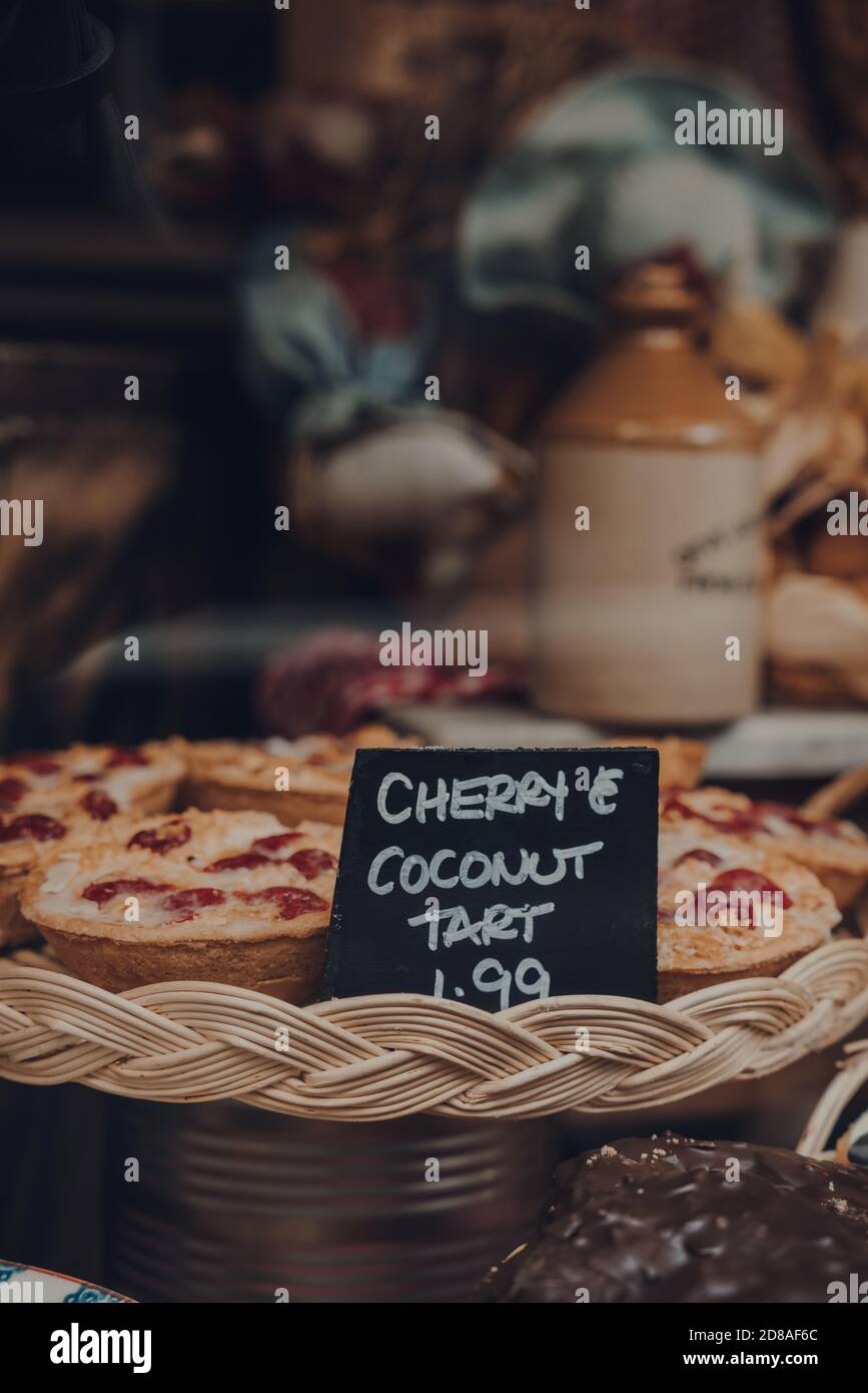 Blick durch das Fenster von frischen Kirsch- und Kokosnusstartes auf einer Verkaufsanzeige einer Bäckerei in Frome, Großbritannien, flacher Fokus. Stockfoto