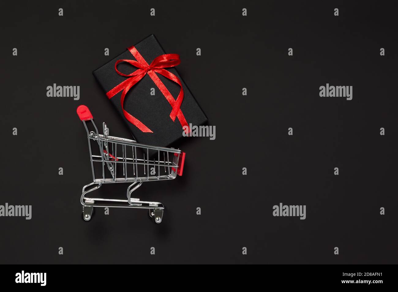 Black Friday Verkaufskonzept. Schwarzes Geschenk mit rotem Band im Warenkorb auf dunklem Hintergrund. Weihnachtseinkäufe, St. Valentin Stockfoto