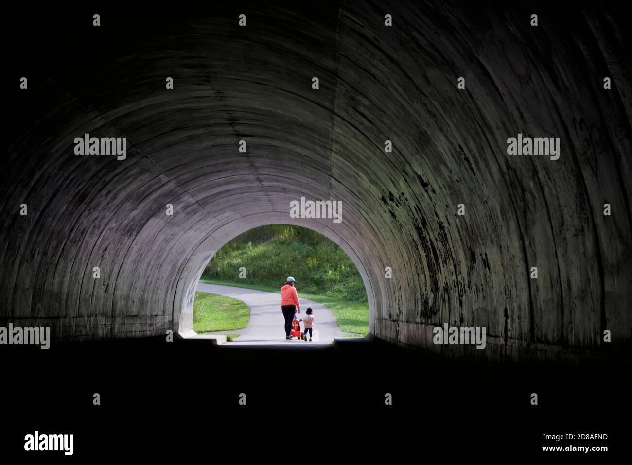 Mutter und Kind, die aus einem dunklen Tunnel in Richtung Ein öffentlicher Park Stockfoto