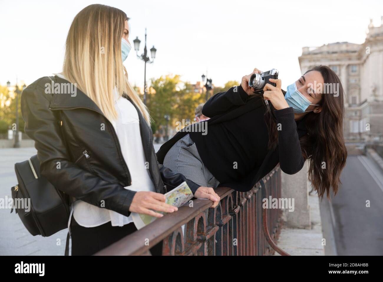 Ein Mädchen, das mit einer analogen Kamera ein Foto von ihrer Freundin gemacht hat. Beide tragen Gesichtsmasken. Konzept der neuen Normalität. Stockfoto