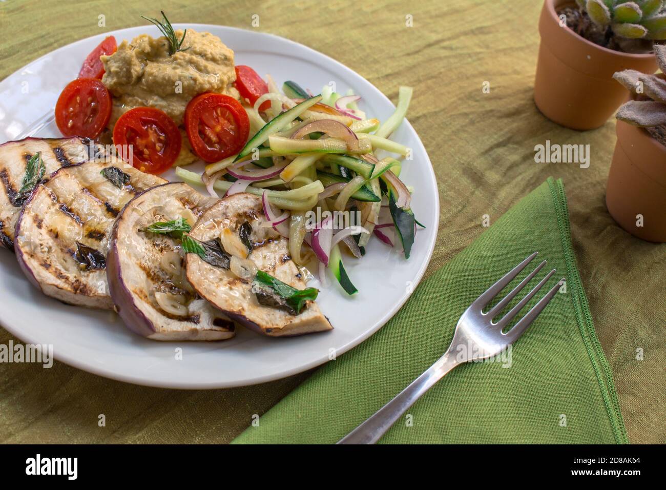 Ein veganes Gericht mit gegrillten tunesischen Auberginen, Kichererbsen-Hummus, Datterini-Tomaten und Julienne-Gurken und Zwiebeln Stockfoto