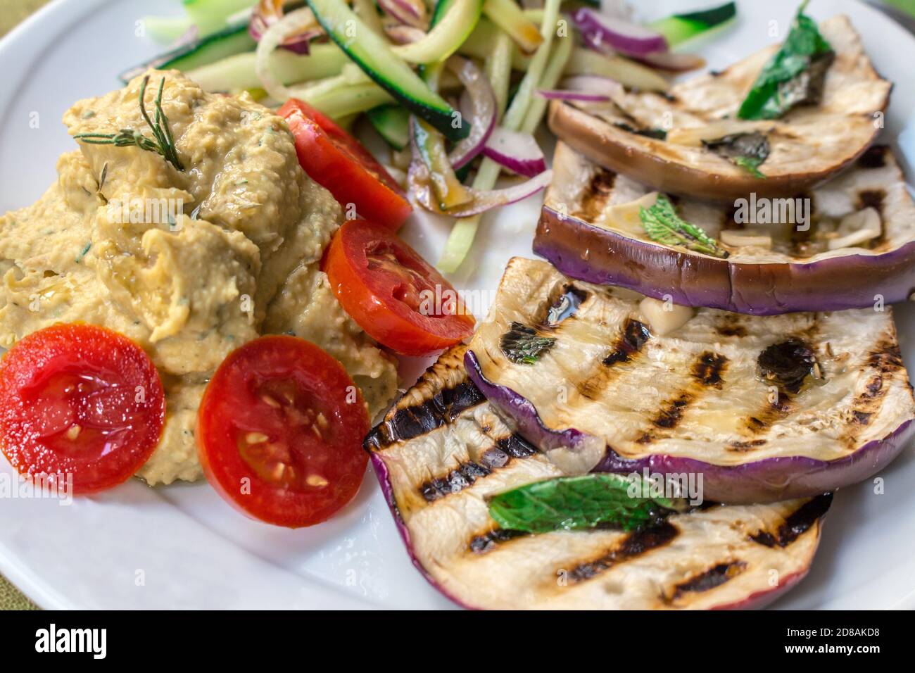 Ein veganes Gericht mit gegrillten tunesischen Auberginen, Kichererbsen-Hummus, Datterini-Tomaten und Julienne-Gurken und Zwiebeln Stockfoto