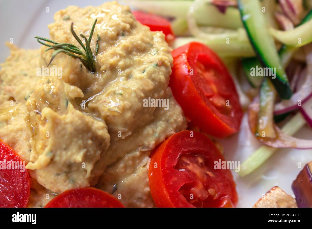 Detail eines veganen Gerichts mit Kichererbsen-Hummus, Datterini-Tomaten und Julienne-Gurken und Zwiebeln Stockfoto