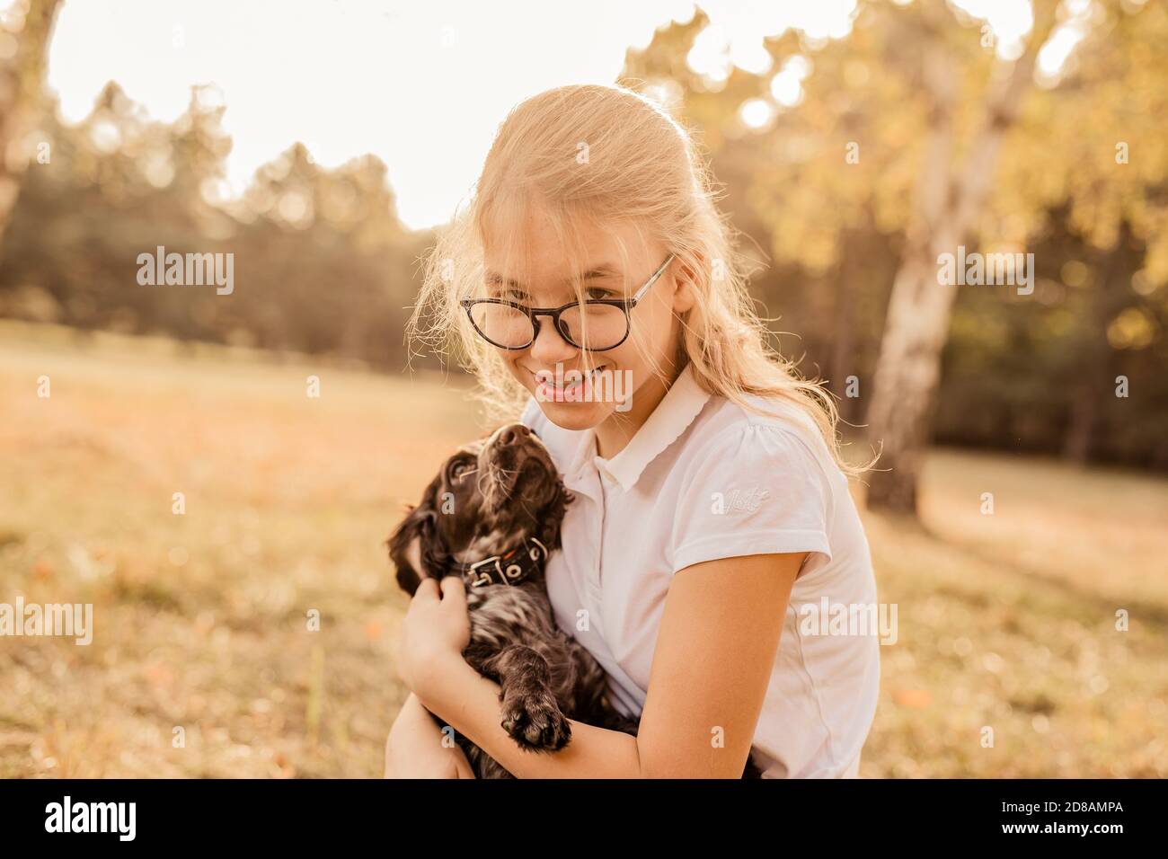 Teenager blonde Mädchen mit großen Gläsern lachen und spielen mit kleinen Welpen Spaniel im warmen Park. Stockfoto