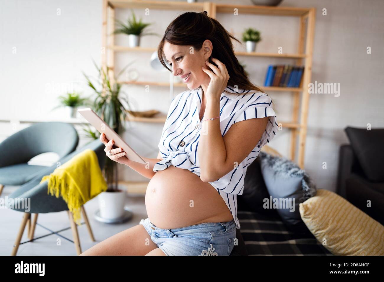 Schöne schwangere Frau mit Tablet-pc zu Hause und entspannend Stockfoto