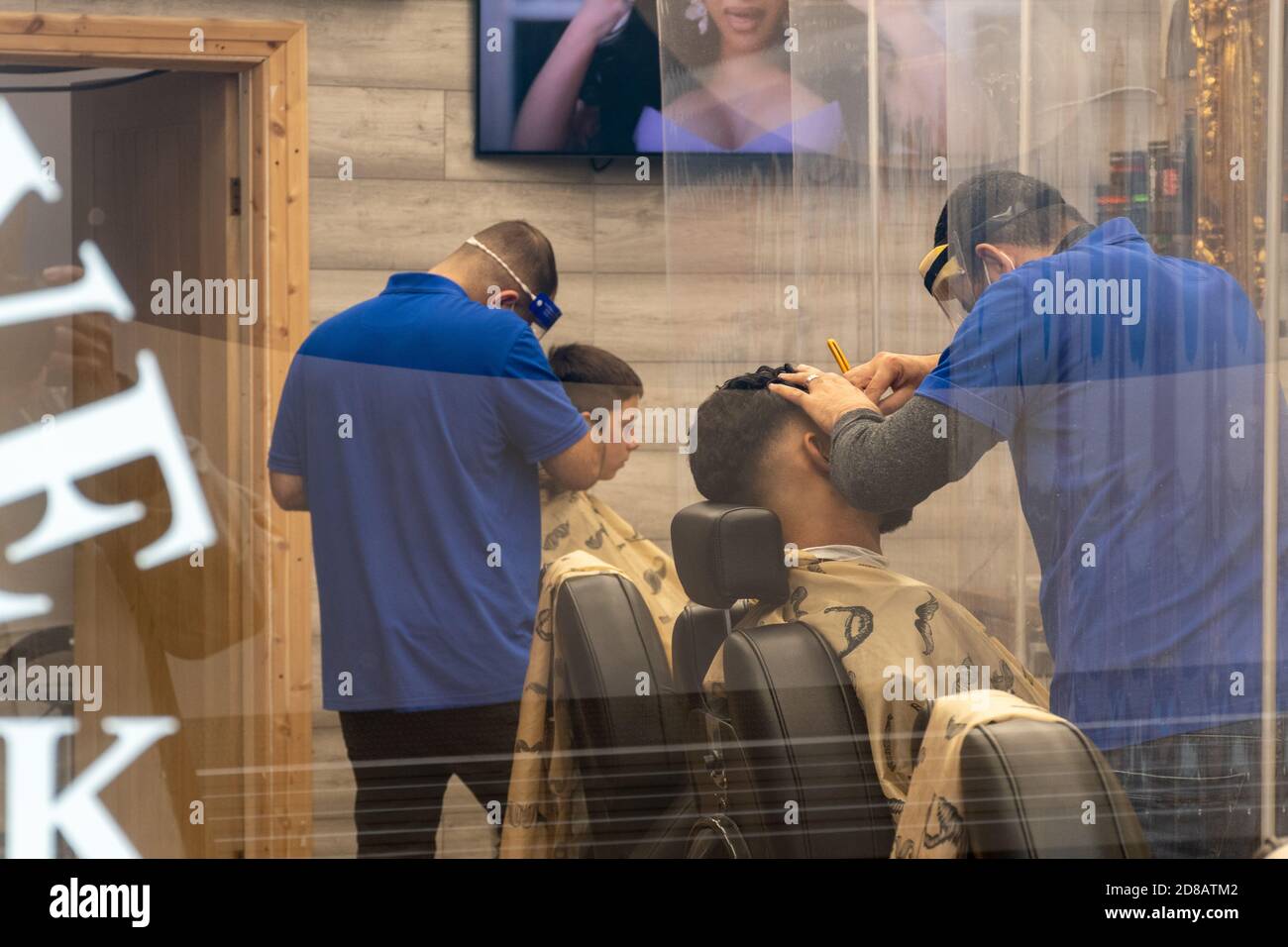 Barbiere, die bei der Pandemie des Covid-19-Coronavirus 2020 in Großbritannien mit sicheren Sicherheitsvorkehrungen im Geschäftsbetrieb arbeiten und Gesichtsschutz tragen. Die neue Normalität. Stockfoto
