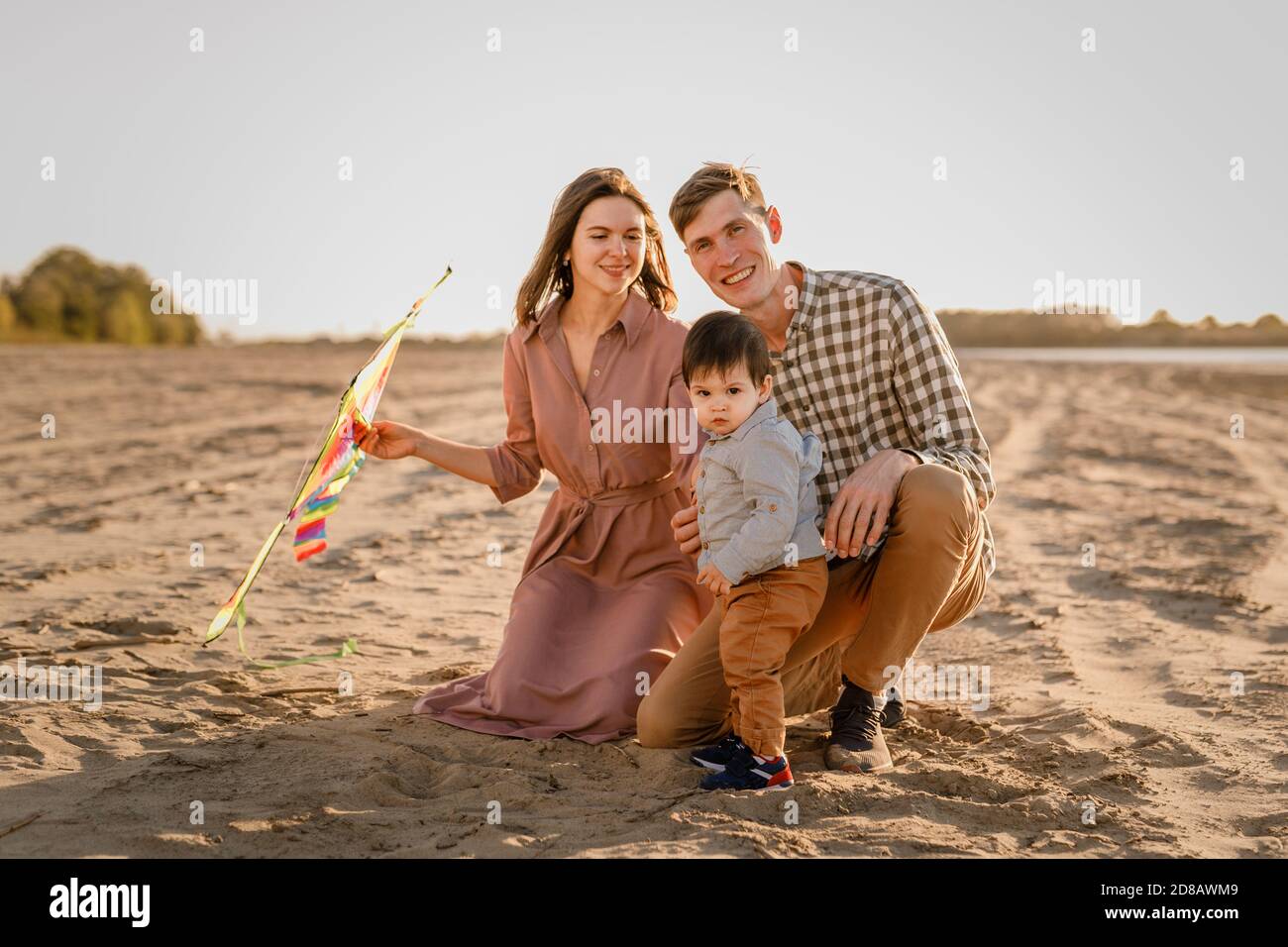 Glückliche Familie zu Fuß am Sandstrand des Flusses. Vater, Mutter hält Baby Sohn auf Händen und spielt mit Drachen Stockfoto